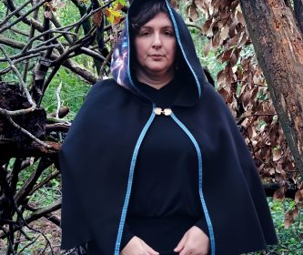 Vue de face d'une cape artisanale noire en laine et polyester avec un brandebourg doré amovible et un liseré en galon bleu.