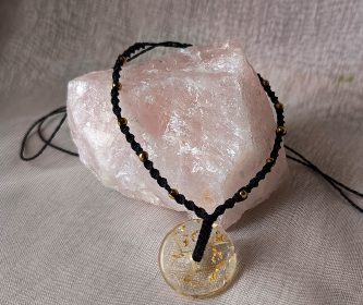Collier artisanal noir posé sur une pierre de quartz rose, montrant le donut résine avec inclusions de pissenlit et feuille d'or.