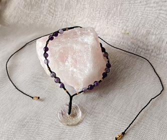 Collier artisanal présenté sur un bloc de quartz rose, mettant en valeur la transparence du donut.
