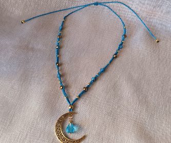 Gros plan sur la lune dorée et sa goutte facettée bleue au cœur du tissage.
