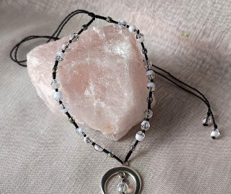 Collier artisanal posé sur un bloc de quartz rose mettant en avant la transparence des perles.