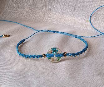 Détail du tissage en micro-macramé turquoise et nœud coulissant réglable posé à plat sur tissu beige.