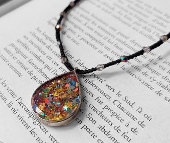 Gros plan du pendentif goutte résine aux paillettes holographiques posé sur les pages d'un livre ancien.
