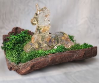 Licorne transparente en résine avec fleurs de glycine séchées sur un socle en écorce d'arbre naturelle et mousse verte.