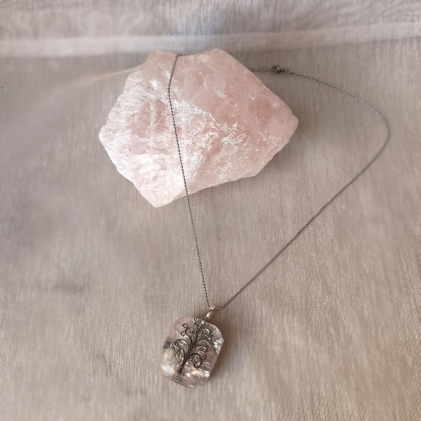 Vue d'ensemble du collier argenté avec sa chaîne fine et son pendentif Arbre de Vie sur tissu beige.