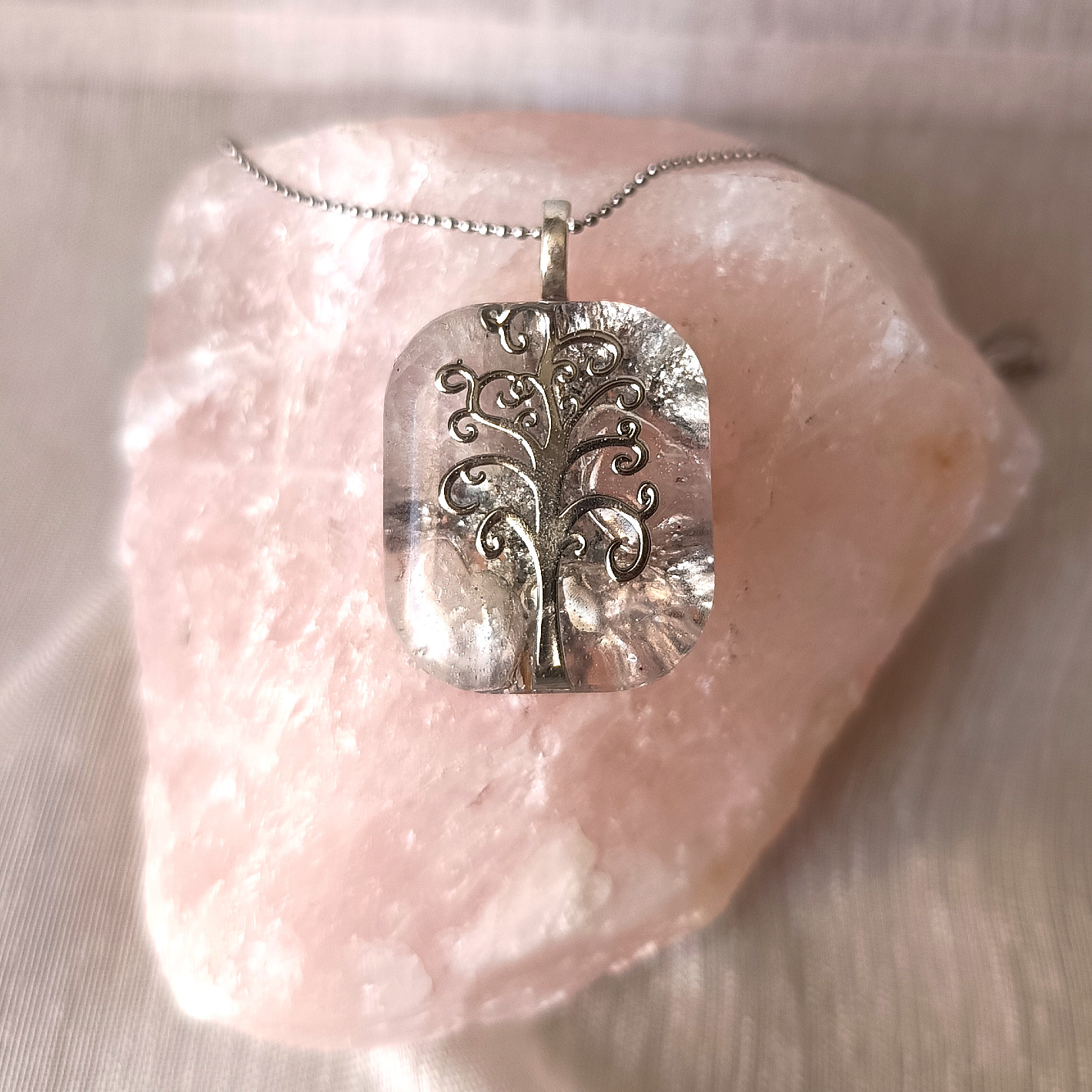 Pendentif en résine Arbre de Vie posé sur un bloc de pierre naturelle de quartz rose brut.