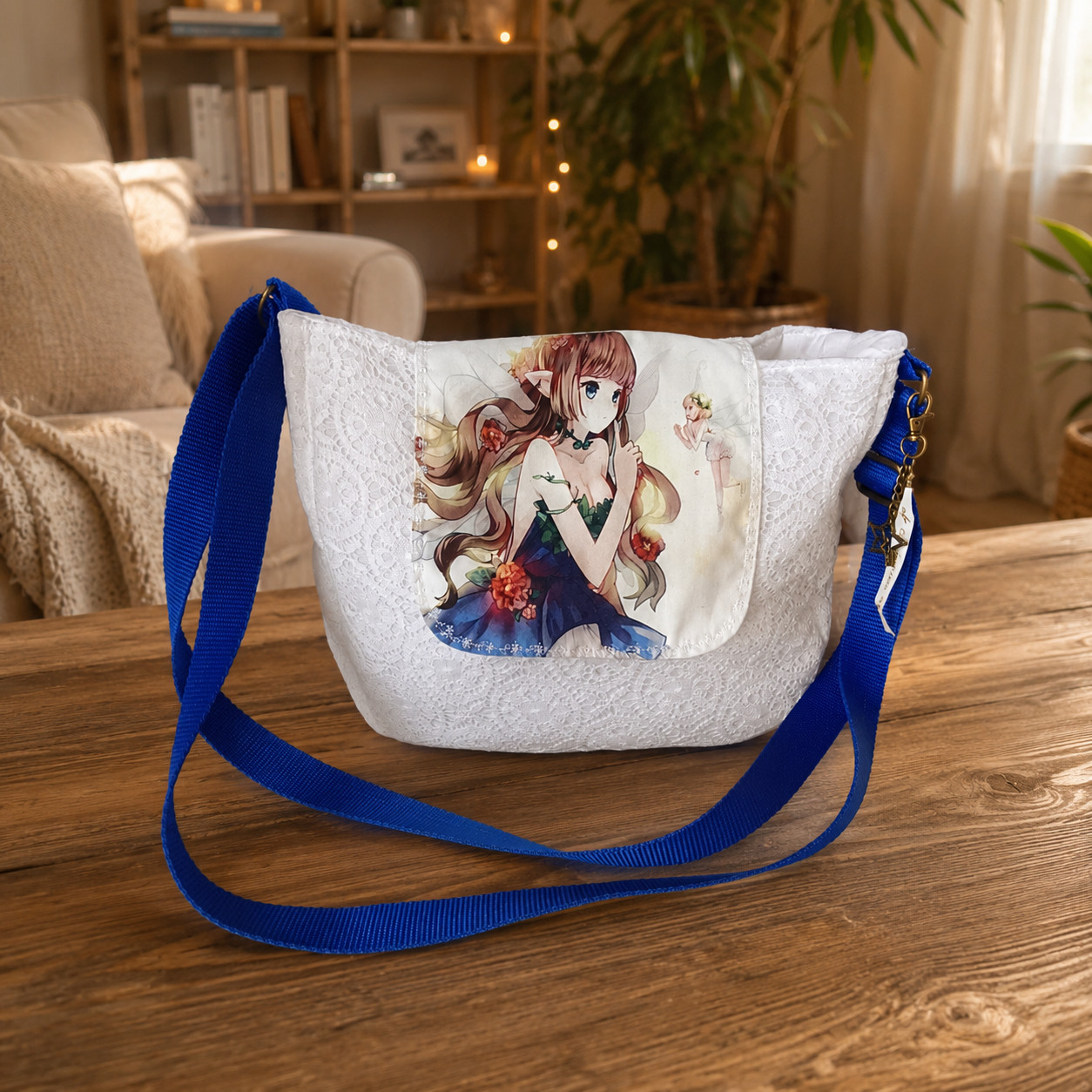 Sac bandoulière Kréa Chic en dentelle blanche avec rabat imprimé fée bleue et sangle bleue posé sur une table en bois.